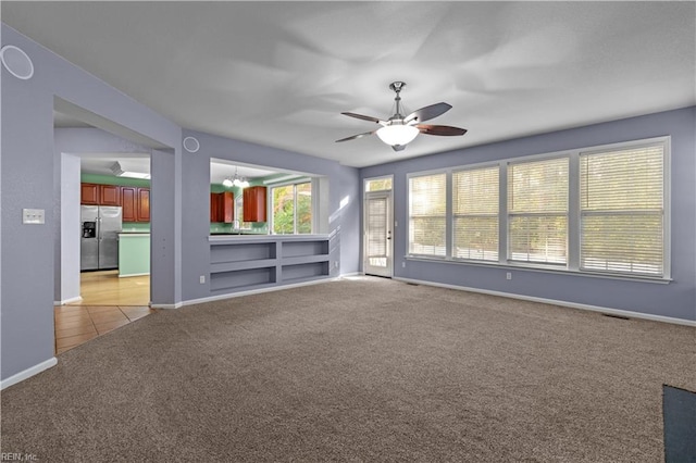 unfurnished living room featuring ceiling fan with notable chandelier, light carpet, and built in shelves