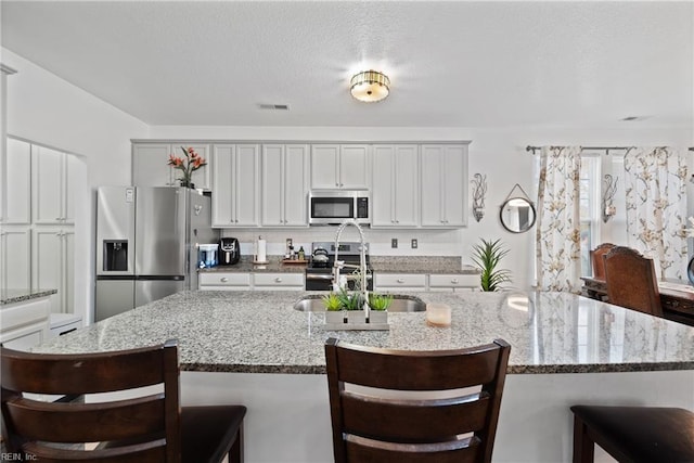 kitchen with a kitchen breakfast bar, light stone countertops, a kitchen island with sink, and appliances with stainless steel finishes