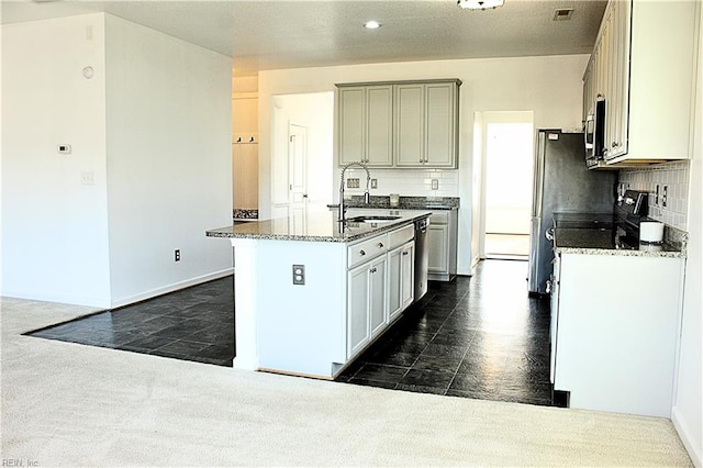 kitchen featuring appliances with stainless steel finishes, tasteful backsplash, a kitchen island with sink, sink, and dark stone countertops