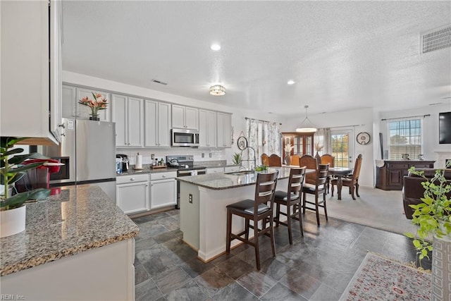 kitchen with pendant lighting, a kitchen island with sink, a kitchen bar, white cabinetry, and stainless steel appliances