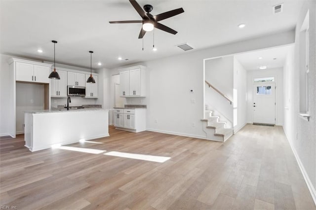 kitchen featuring white cabinets, light wood-type flooring, a kitchen island with sink, and decorative light fixtures