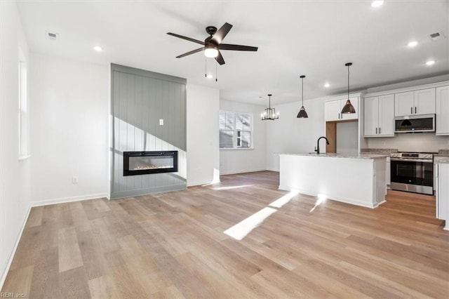 kitchen with appliances with stainless steel finishes, hanging light fixtures, an island with sink, light hardwood / wood-style floors, and white cabinets