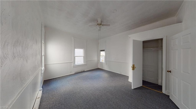 unfurnished bedroom with a closet, dark carpet, ceiling fan, and a baseboard heating unit