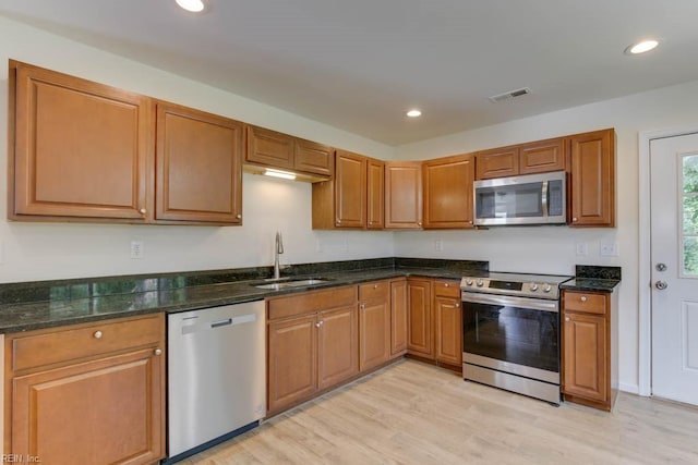 kitchen with light wood-type flooring, appliances with stainless steel finishes, sink, and dark stone countertops