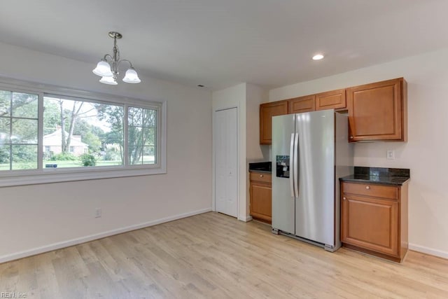 kitchen featuring dark stone countertops, decorative light fixtures, a notable chandelier, stainless steel fridge with ice dispenser, and light wood-type flooring