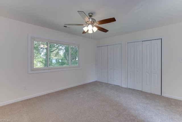 unfurnished bedroom featuring ceiling fan, light carpet, and two closets