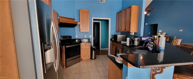 kitchen with light tile patterned flooring, extractor fan, sink, appliances with stainless steel finishes, and a breakfast bar area