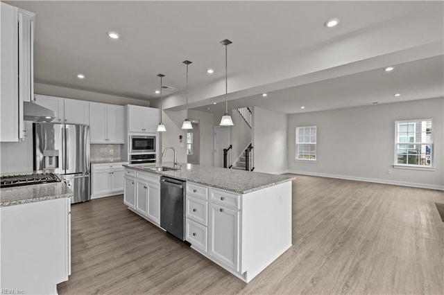 kitchen featuring appliances with stainless steel finishes, decorative light fixtures, light hardwood / wood-style flooring, white cabinetry, and an island with sink