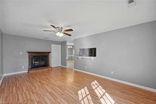 unfurnished living room with light wood-type flooring, a fireplace, and ceiling fan with notable chandelier