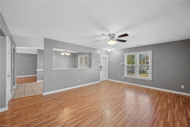 spare room with ceiling fan with notable chandelier and light hardwood / wood-style flooring