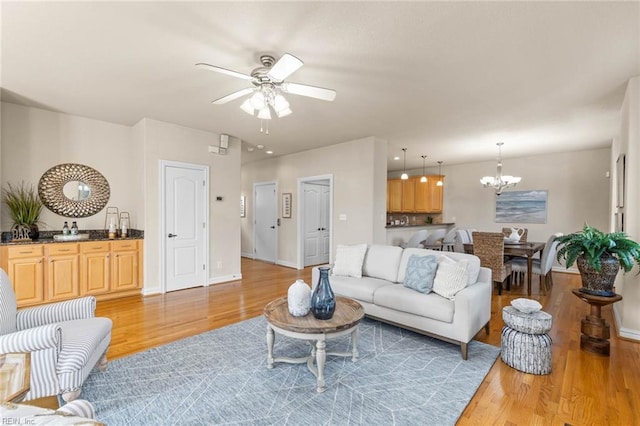 living room with ceiling fan with notable chandelier and light hardwood / wood-style flooring