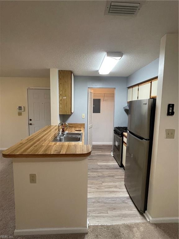 kitchen with light hardwood / wood-style floors, kitchen peninsula, sink, gas stove, and stainless steel refrigerator