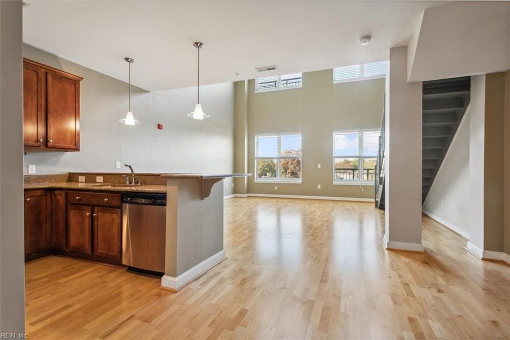 kitchen featuring dishwasher, a kitchen breakfast bar, sink, hanging light fixtures, and light wood-type flooring