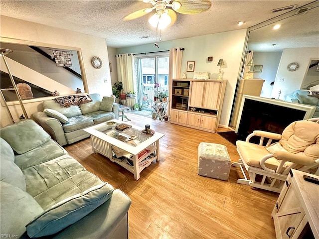 living room featuring light wood-type flooring, a textured ceiling, and ceiling fan