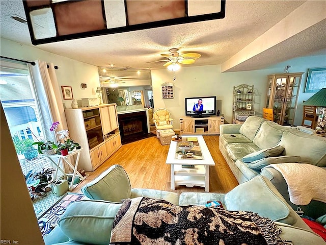 living room featuring light wood-type flooring, a textured ceiling, and ceiling fan