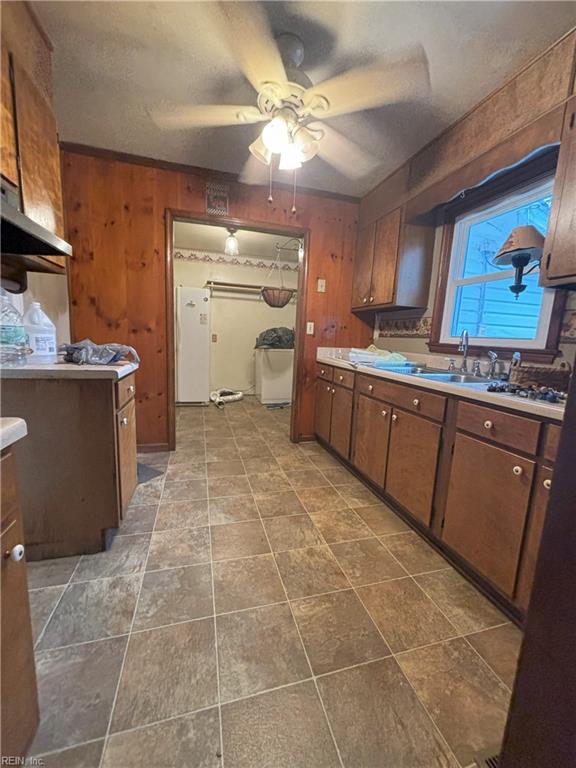 kitchen featuring white fridge, wooden walls, sink, and ceiling fan