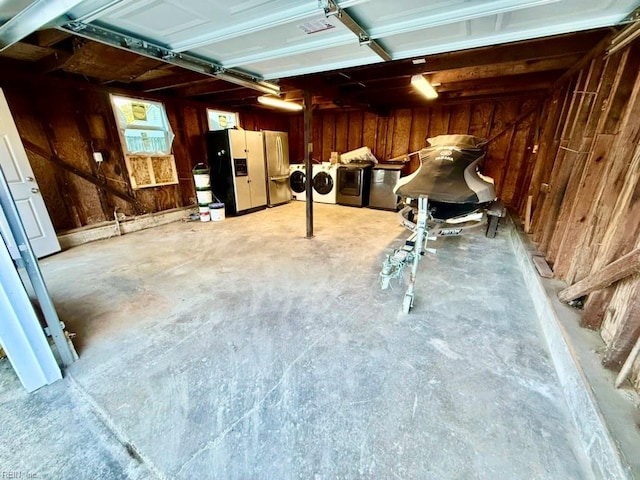 garage with white fridge with ice dispenser, washing machine and dryer, wooden walls, and stainless steel fridge