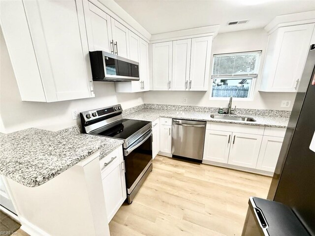 kitchen with light hardwood / wood-style flooring, sink, light stone countertops, white cabinetry, and appliances with stainless steel finishes