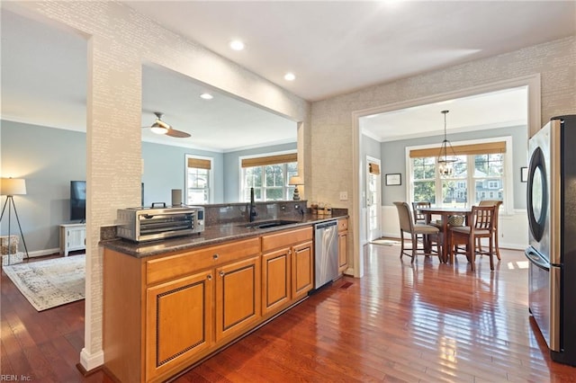 kitchen with a sink, appliances with stainless steel finishes, brown cabinets, decorative light fixtures, and crown molding