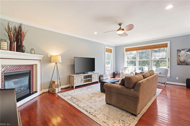 living area featuring baseboards, a tiled fireplace, dark wood-style floors, crown molding, and recessed lighting