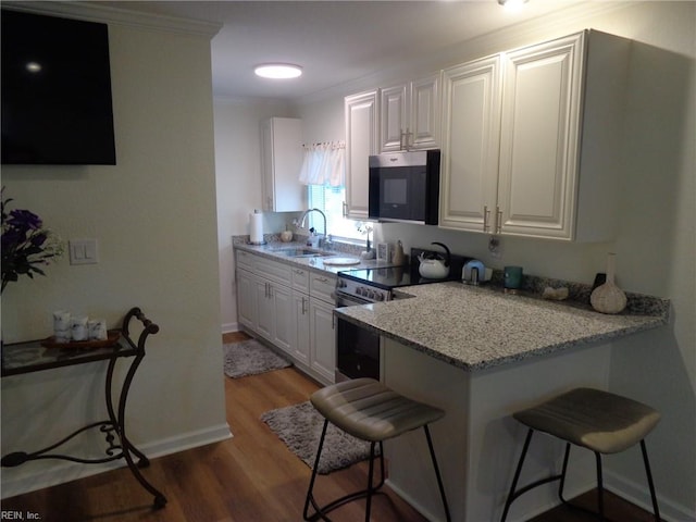 kitchen featuring light stone counters, appliances with stainless steel finishes, white cabinets, sink, and a breakfast bar area