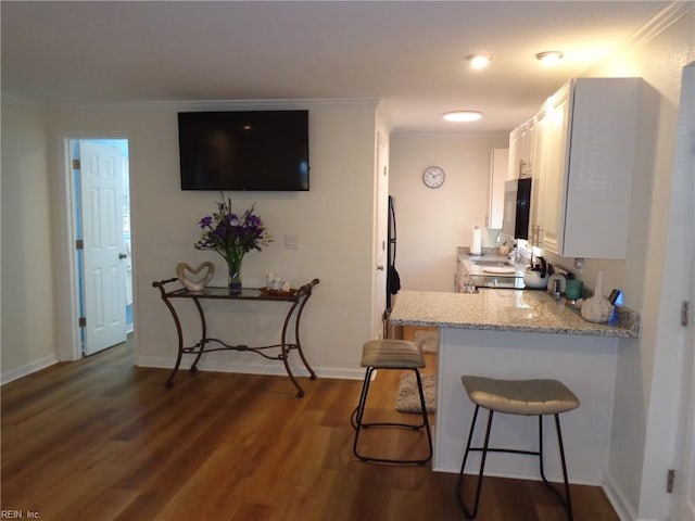 kitchen featuring dark wood-type flooring, a breakfast bar area, ornamental molding, light stone countertops, and white cabinetry