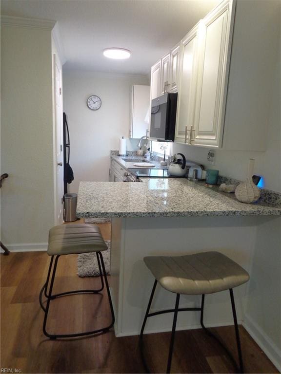 kitchen with light stone countertops, kitchen peninsula, a kitchen breakfast bar, and white cabinets