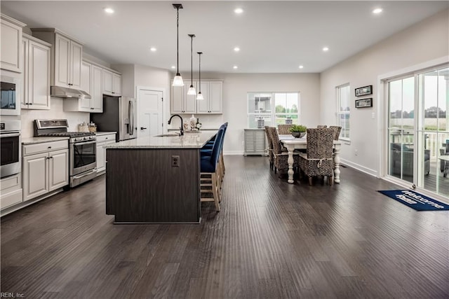 kitchen featuring a center island with sink, appliances with stainless steel finishes, dark hardwood / wood-style floors, hanging light fixtures, and a kitchen breakfast bar