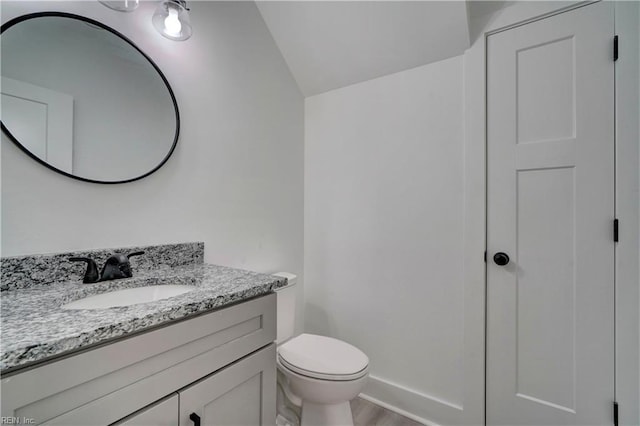 bathroom with toilet, vanity, vaulted ceiling, and wood-type flooring