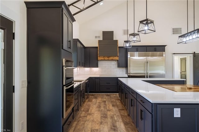 kitchen featuring stainless steel appliances, backsplash, decorative light fixtures, wood-type flooring, and a barn door