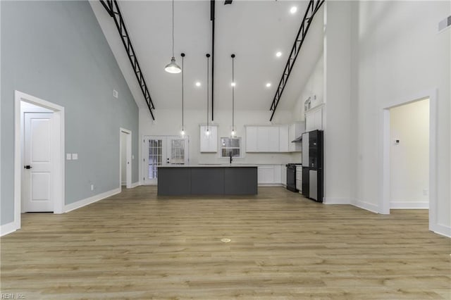 kitchen with a center island with sink, white cabinets, black appliances, hanging light fixtures, and a high ceiling