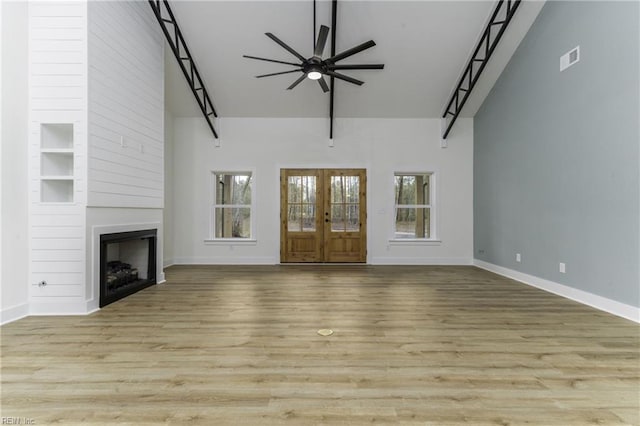 unfurnished living room with plenty of natural light, light wood-type flooring, ceiling fan, and a towering ceiling