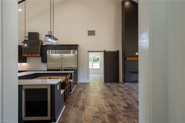 kitchen featuring wine cooler, backsplash, a barn door, dark wood-type flooring, and stainless steel built in refrigerator