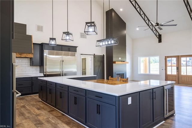 kitchen with stainless steel built in fridge, dark wood-type flooring, a barn door, a kitchen island, and a high ceiling