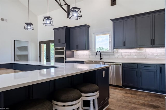 kitchen featuring stainless steel appliances, high vaulted ceiling, hanging light fixtures, dark wood-type flooring, and decorative backsplash