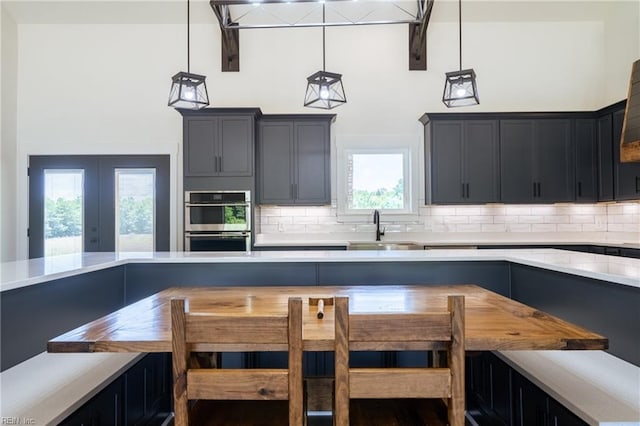 kitchen featuring a healthy amount of sunlight, hanging light fixtures, sink, tasteful backsplash, and stainless steel double oven