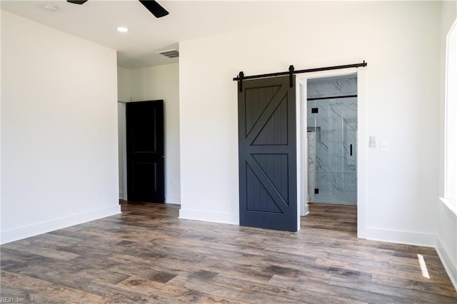 unfurnished bedroom with dark hardwood / wood-style flooring, a barn door, ceiling fan, and ensuite bathroom