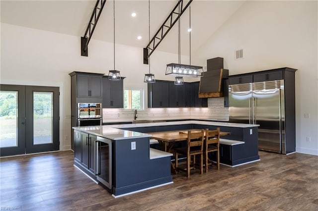 kitchen with stainless steel appliances, a center island, hanging light fixtures, high vaulted ceiling, and wine cooler