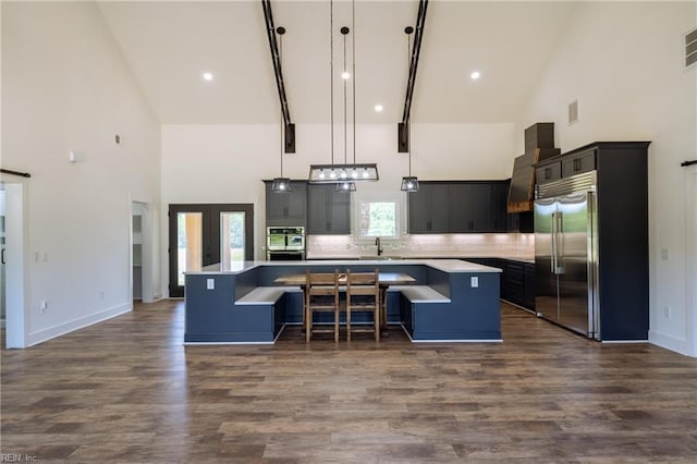 kitchen with dark wood-type flooring, hanging light fixtures, high vaulted ceiling, a kitchen island, and appliances with stainless steel finishes