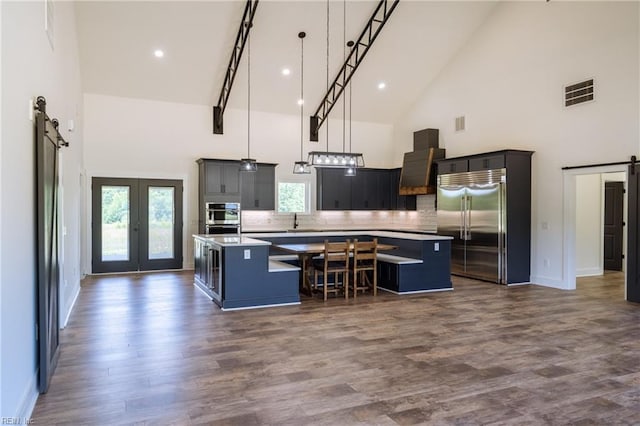 kitchen with a barn door, high vaulted ceiling, a kitchen island, extractor fan, and appliances with stainless steel finishes