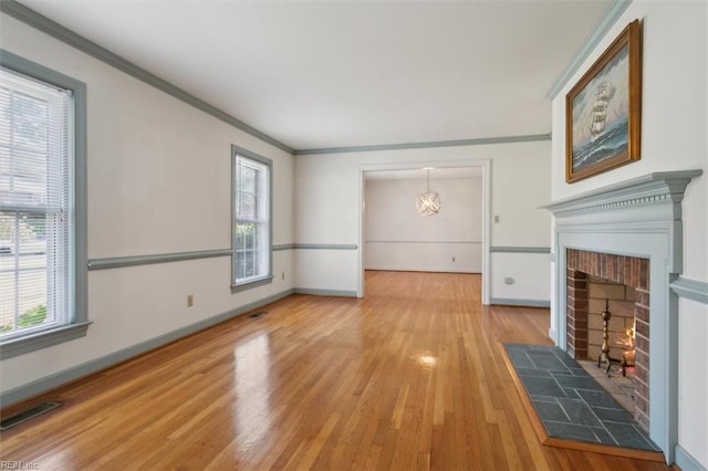 unfurnished living room with plenty of natural light, hardwood / wood-style flooring, ornamental molding, and a brick fireplace