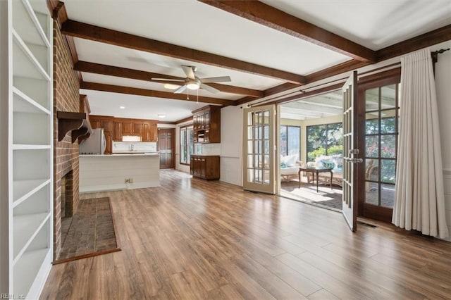 unfurnished living room with hardwood / wood-style flooring, ceiling fan, beam ceiling, a brick fireplace, and french doors