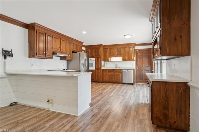 kitchen with crown molding, appliances with stainless steel finishes, sink, light hardwood / wood-style floors, and kitchen peninsula