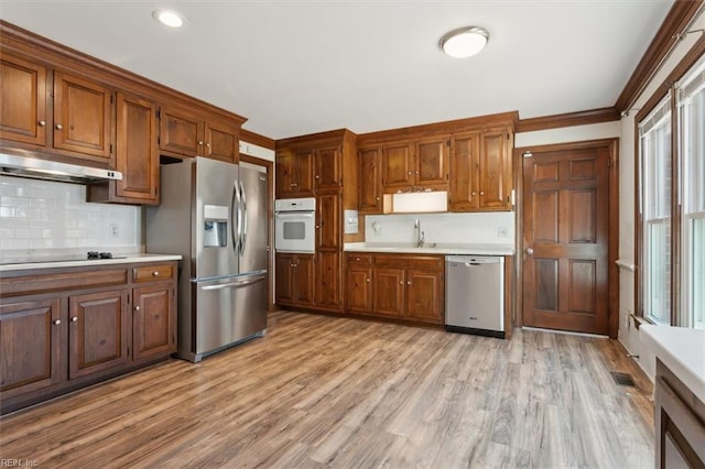 kitchen with light hardwood / wood-style floors, sink, appliances with stainless steel finishes, ornamental molding, and backsplash