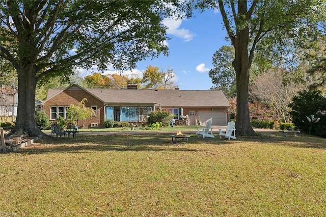 rear view of house featuring a garage, a lawn, and an outdoor fire pit