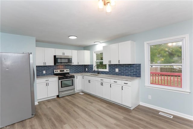 kitchen featuring white cabinetry, appliances with stainless steel finishes, light stone countertops, sink, and light hardwood / wood-style floors