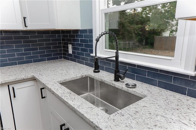 kitchen featuring white cabinets, sink, light stone counters, and backsplash