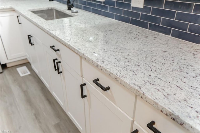 details featuring light stone counters, white cabinets, sink, backsplash, and light hardwood / wood-style flooring