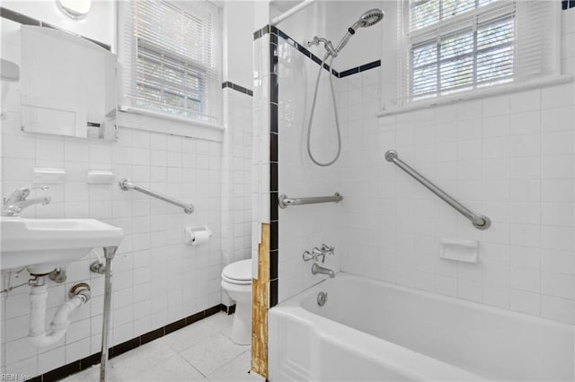 bathroom with tile patterned flooring, tiled shower / bath, toilet, and tile walls