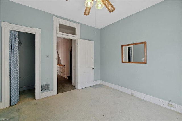 unfurnished bedroom with a walk in closet, a closet, light colored carpet, and ceiling fan